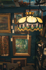 Vintage-style lamp with beaded shade hanging among framed paintings on a blue wall.
