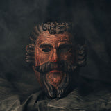 Dark, textured antique wood mask with intricate details on a dark background