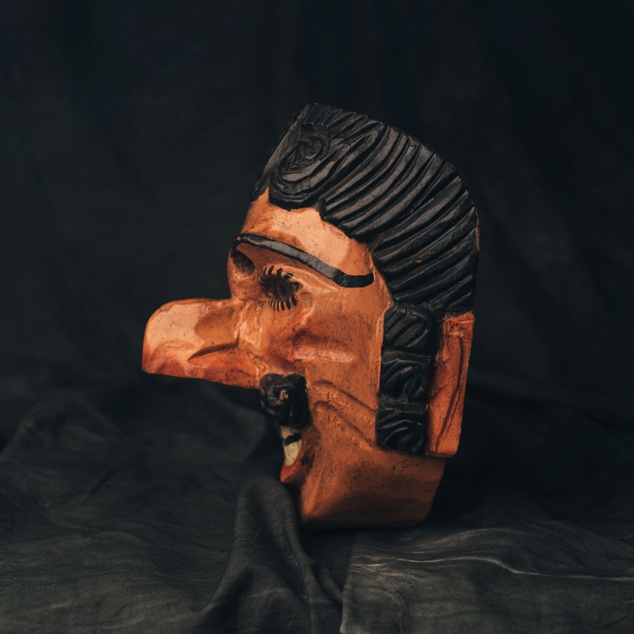 Side view of a wooden 18th Century Guatemalan mask with intricate carvings on a dark background