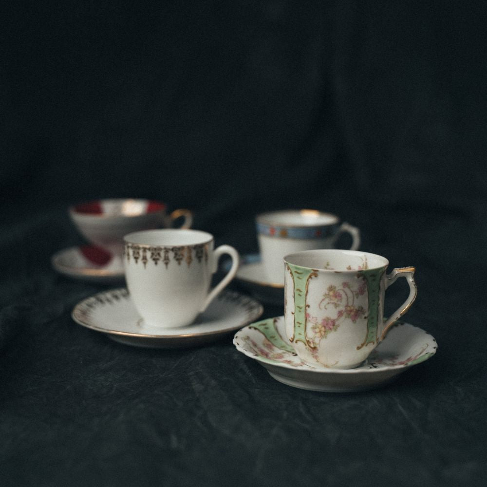 Four vintage demitasse cup and saucer sets arranged in soft light, each with unique silhouettes and intricate detailing.