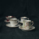 Four vintage demitasse cup and saucer sets arranged in soft light, each with unique silhouettes and intricate detailing.