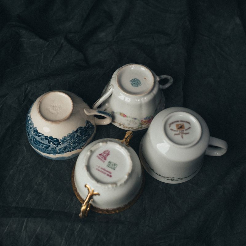 Bottom view of mismatched vintage saucers showing maker’s marks, glaze wear, and signs of their well-traveled past.