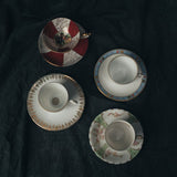 Close-up of vintage demitasse cups showing ornate handles, hand-painted borders, and delicate glaze variations.