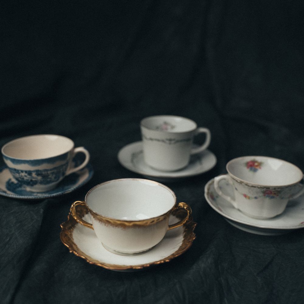 Close-up of vintage teacup rims showing delicate patterns, floral motifs, and gold embellishments across a curated mismatched collection.