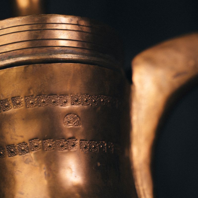 Detailed close-up of hand-engraved floral and geometric patterns on the body of the oldest pot, highlighting its chased ornamentation.