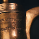 Detailed close-up of hand-engraved floral and geometric patterns on the body of the oldest pot, highlighting its chased ornamentation.