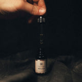 Hand holding the Elixir of Life essential oil dropper, showcasing the golden liquid and precise application for daily rituals.