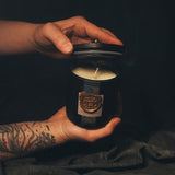 Hands holding the Faire Fortune candle, showing its glass vessel size and ornate label inspired by renaissance opulence.
