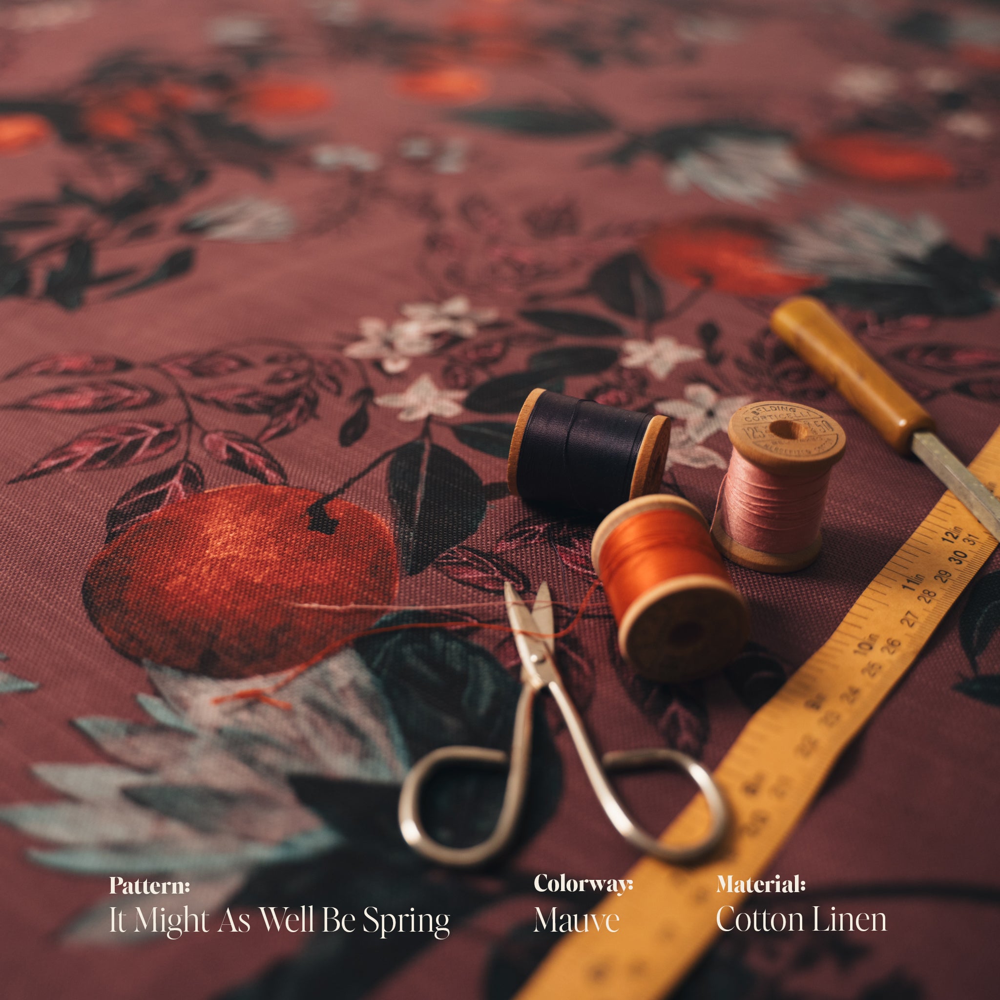 Floral fabric with spools of thread, scissors, and a ruler on a matching patterned background.