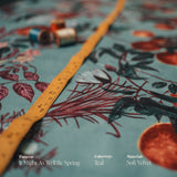 A Teal Floral patterned fabric with a measuring tape, spools of thread, and text describing pattern, colorway, and materials.