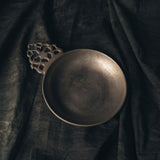 Pewter Porringer bowl with decorative handle on a dark fabric background