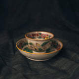 Decorative ceramic cup and saucer with intricate patterns on a dark fabric background