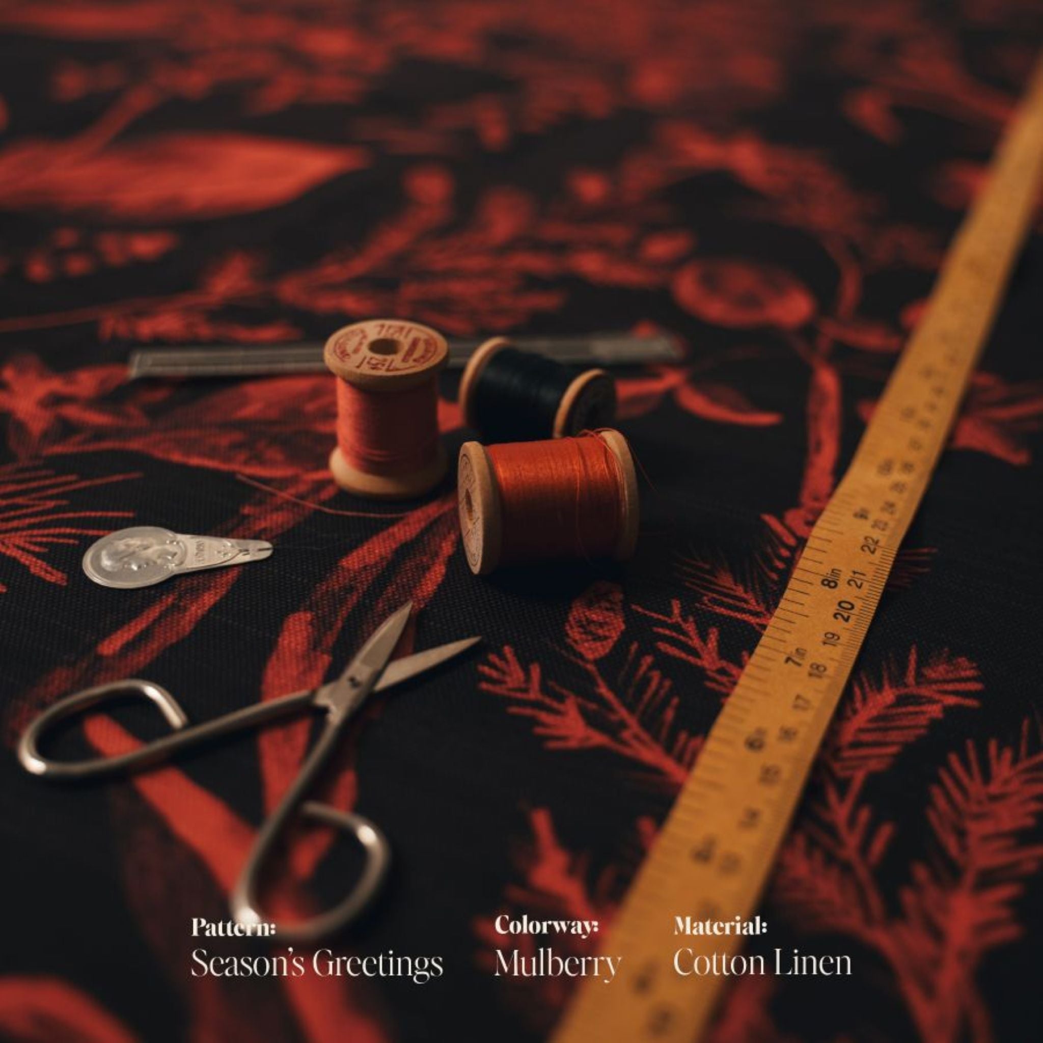 Spools of thread and a ruler on the Seasons Greetings mulberry cotton linen fabric with 'Season's Greetings' text overlay.