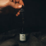 Hand holding the Season's Greetings essential oil dropper above the amber bottle, highlighting golden drops and festive scent notes.