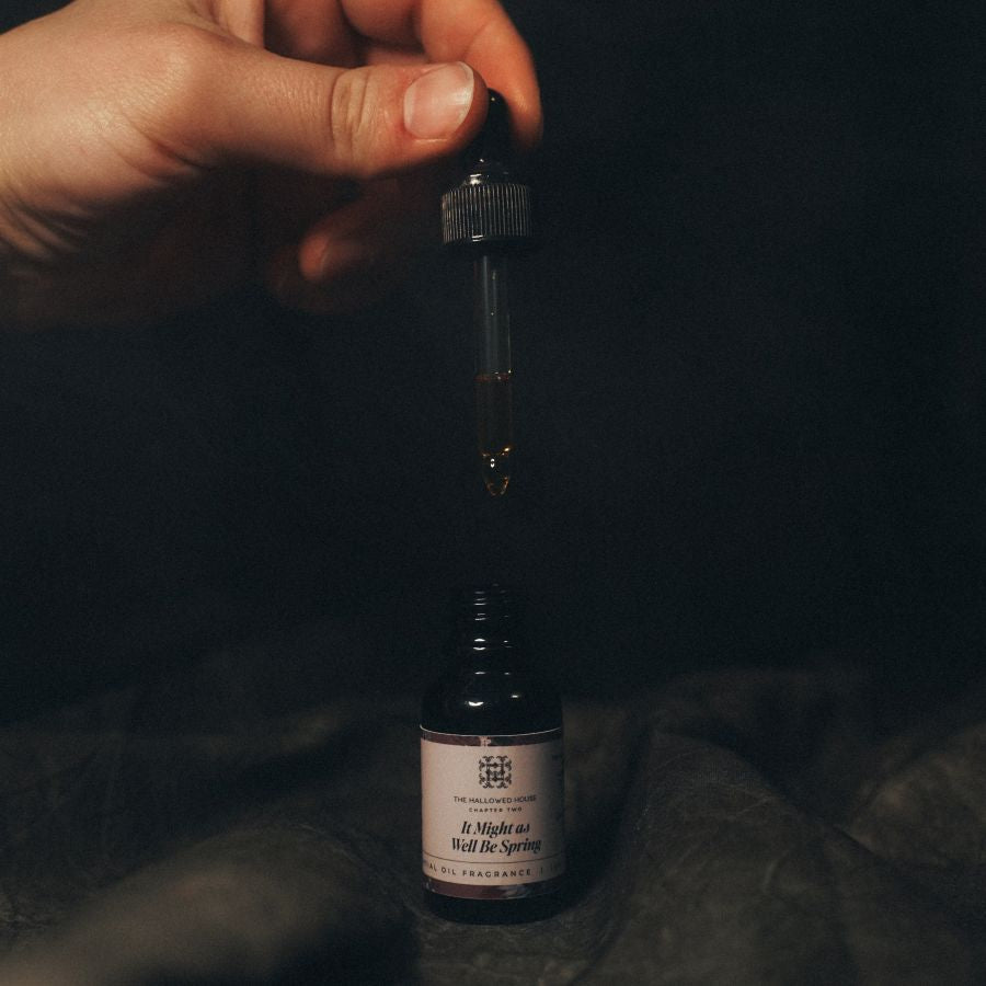 Close-up of a hand using the It Might As Well Be Spring oil dropper above the open amber bottle, capturing the citrusy, floral golden blend.